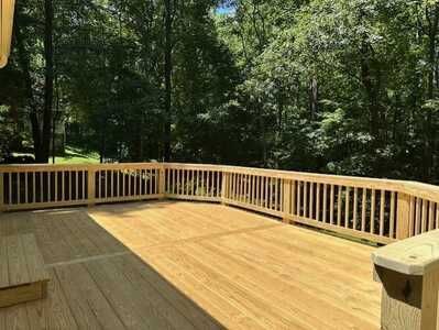 A large wooden deck with a railing and trees in the background.