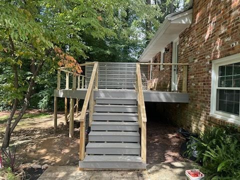 A gray wooden staircase leads up to a deck attached to a brick house.