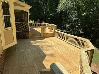 A large wooden deck with a railing in front of a house.