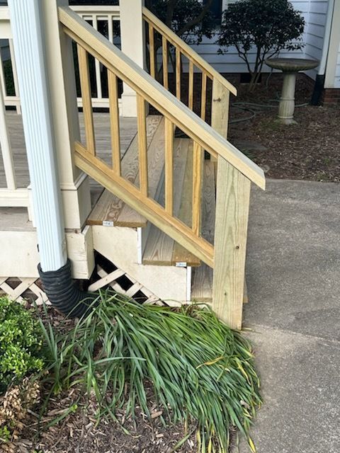 Wooden porch stairs with a newly built handrail, next to a house.