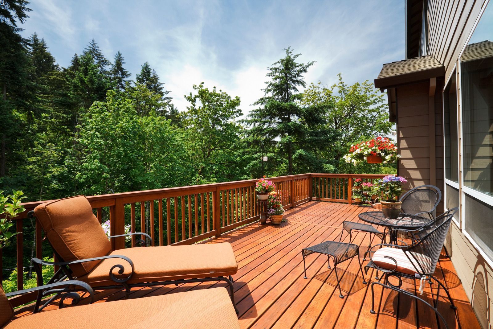 Wooden deck with seating overlooking lush green trees and sky.
