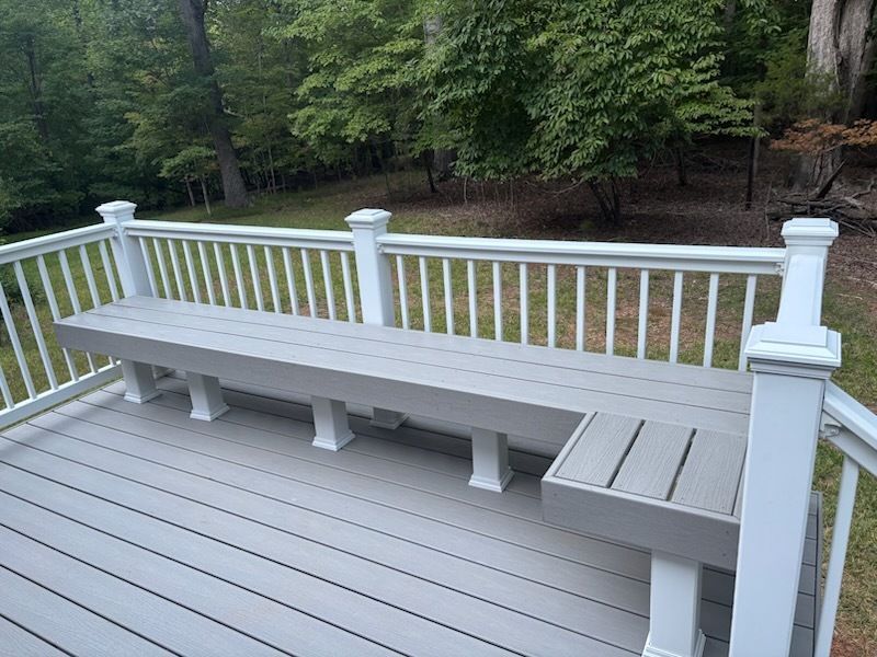 Gray bench on deck with white railing; trees in background.