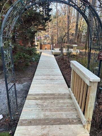 Wooden boardwalk through garden, with arched metal arbor entrance.