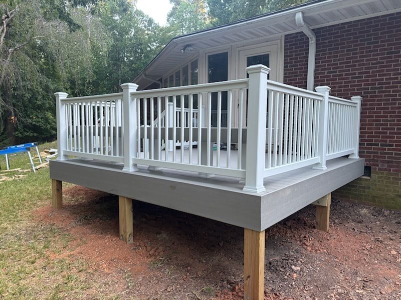 White-railed deck with gray base, supported by wooden posts, in front of a brick house.