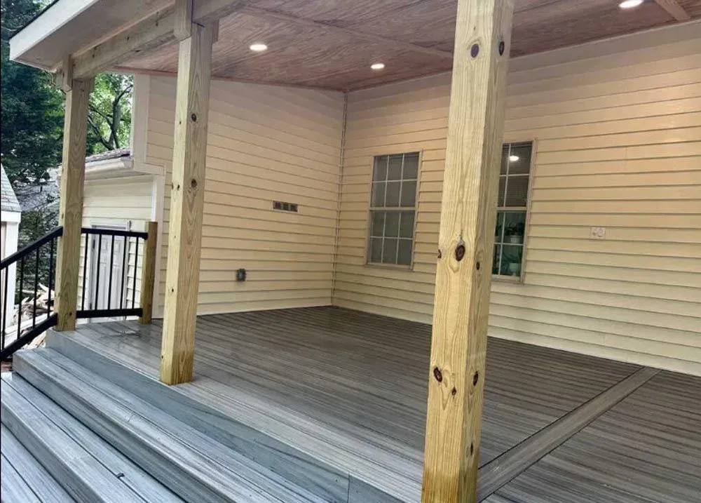 There is a covered porch with a wooden deck and stairs.