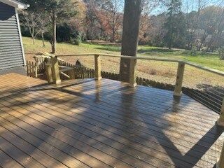 A wooden deck with a railing and a view of a field.