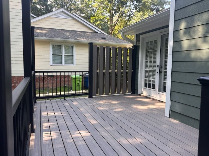 Wooden deck with gray floorboards and black railings, overlooking a backyard with a yellow house.