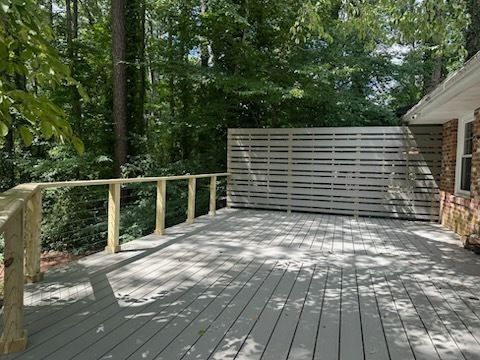 Wooden deck with railing and privacy fence; surrounded by trees and house.
