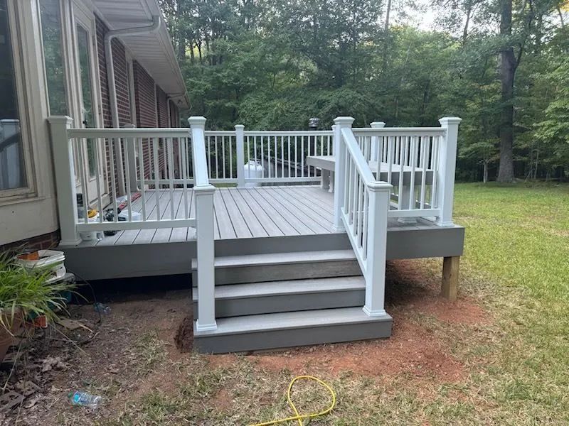 Gray composite deck with white railings, steps, and posts in a grassy backyard.