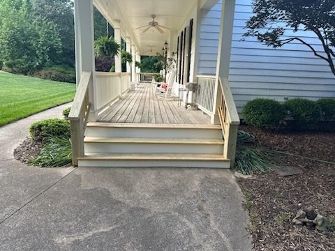 A front porch with steps leading to a covered veranda. Wooden deck and railing, concrete walkway.