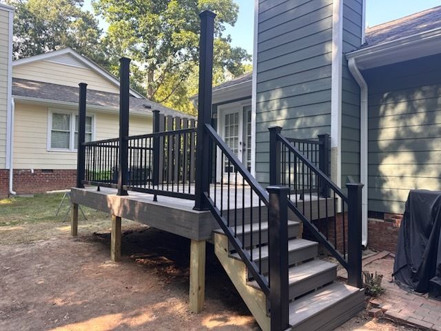 Black-railed deck with steps; dark posts and grey deck boards against a light-yellow and green house exterior.