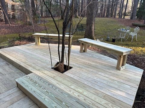 Wooden deck with benches, tree in the center, and outdoor seating in a wooded yard.
