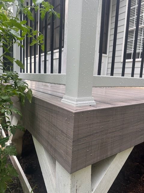 Composite deck corner with white column, railing, and trim. Brown deck boards meet white support beams.