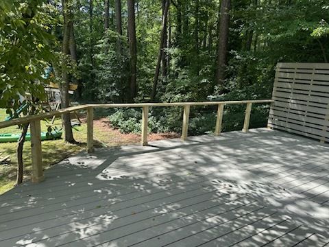 Wooden deck with railing in a wooded setting, painted gray, with light wood railing.