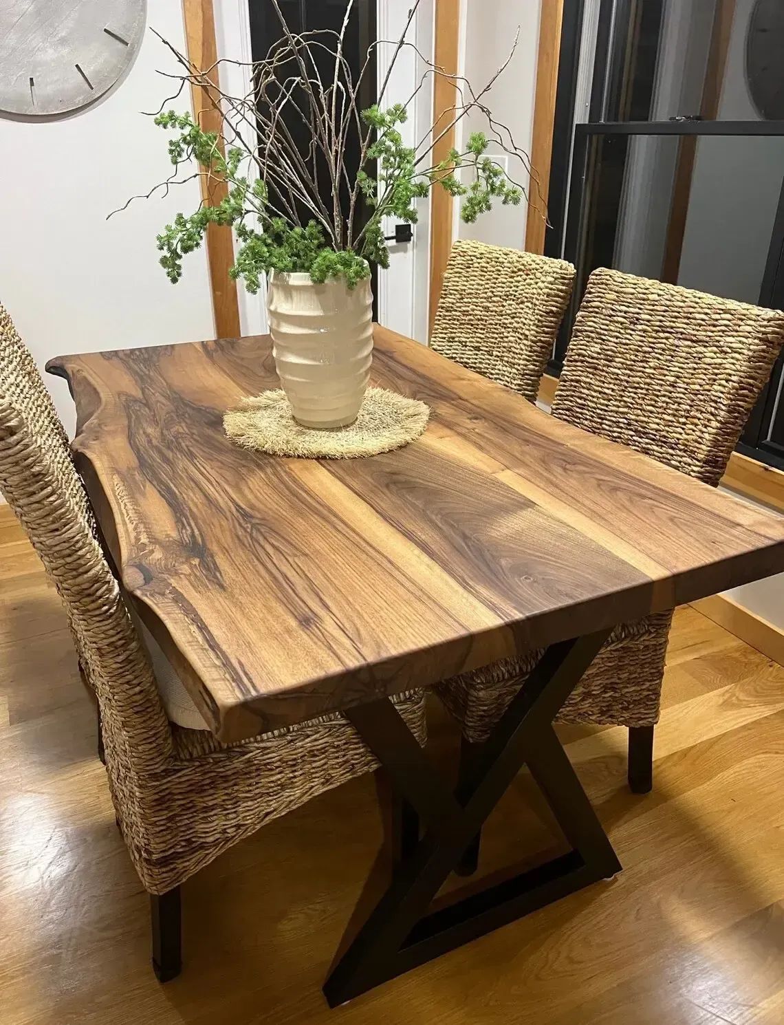 Wooden dining table with woven chairs and a vase centerpiece in a cozy room