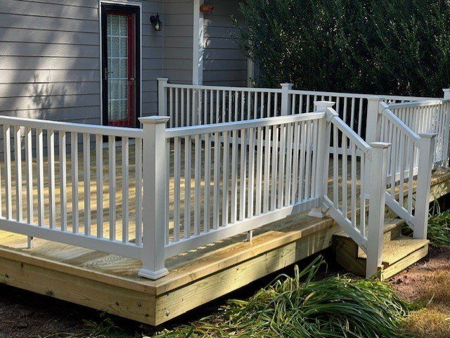 A wooden deck with a white railing and stairs is in front of a house.