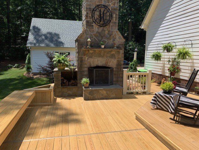 A wooden deck with a fireplace and rocking chairs in front of a house.