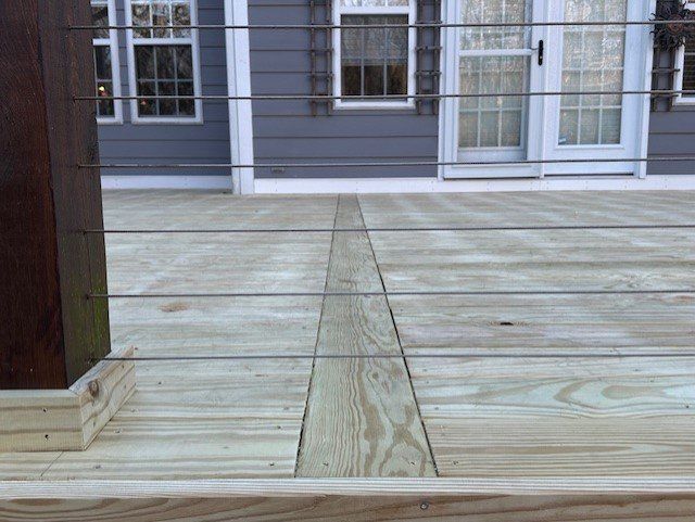 A wooden deck with a stainless steel railing in front of a house.