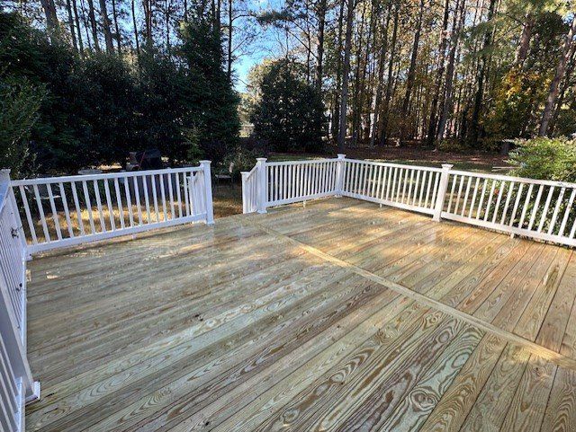 A large wooden deck with a white railing and trees in the background.