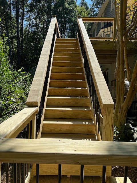 A wooden staircase leading up to a deck with trees in the background.