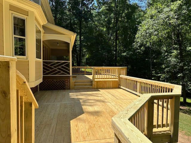 A large wooden deck with stairs and a screened in porch surrounded by trees.