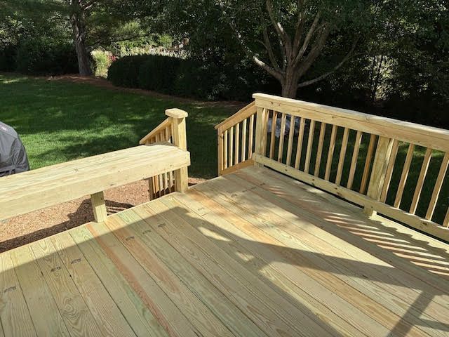 A wooden deck with a bench and stairs in a backyard.