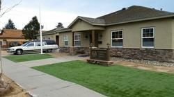 A one-story building with a light-colored exterior and stone accents. A hearse is parked in the driveway.