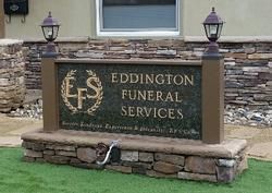 Sign for Eddington Funeral Services. Stone sign with lights, brown pillars, green grass, and stone facade.