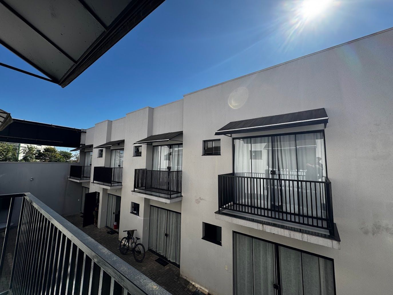 Fileira de edifícios brancos com varandas, grades pretas e céu azul claro.