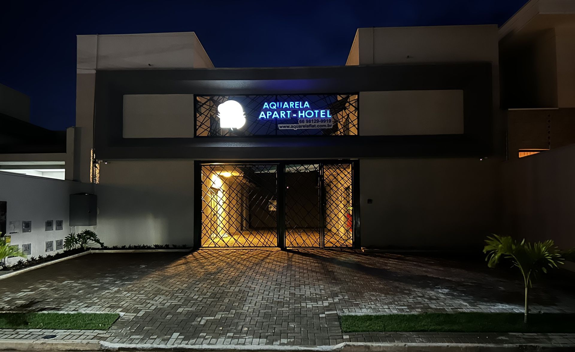 AQ Villa Apart Hotel à noite. Entrada iluminada, letreiro iluminado, fachada escura, entrada pavimentada.