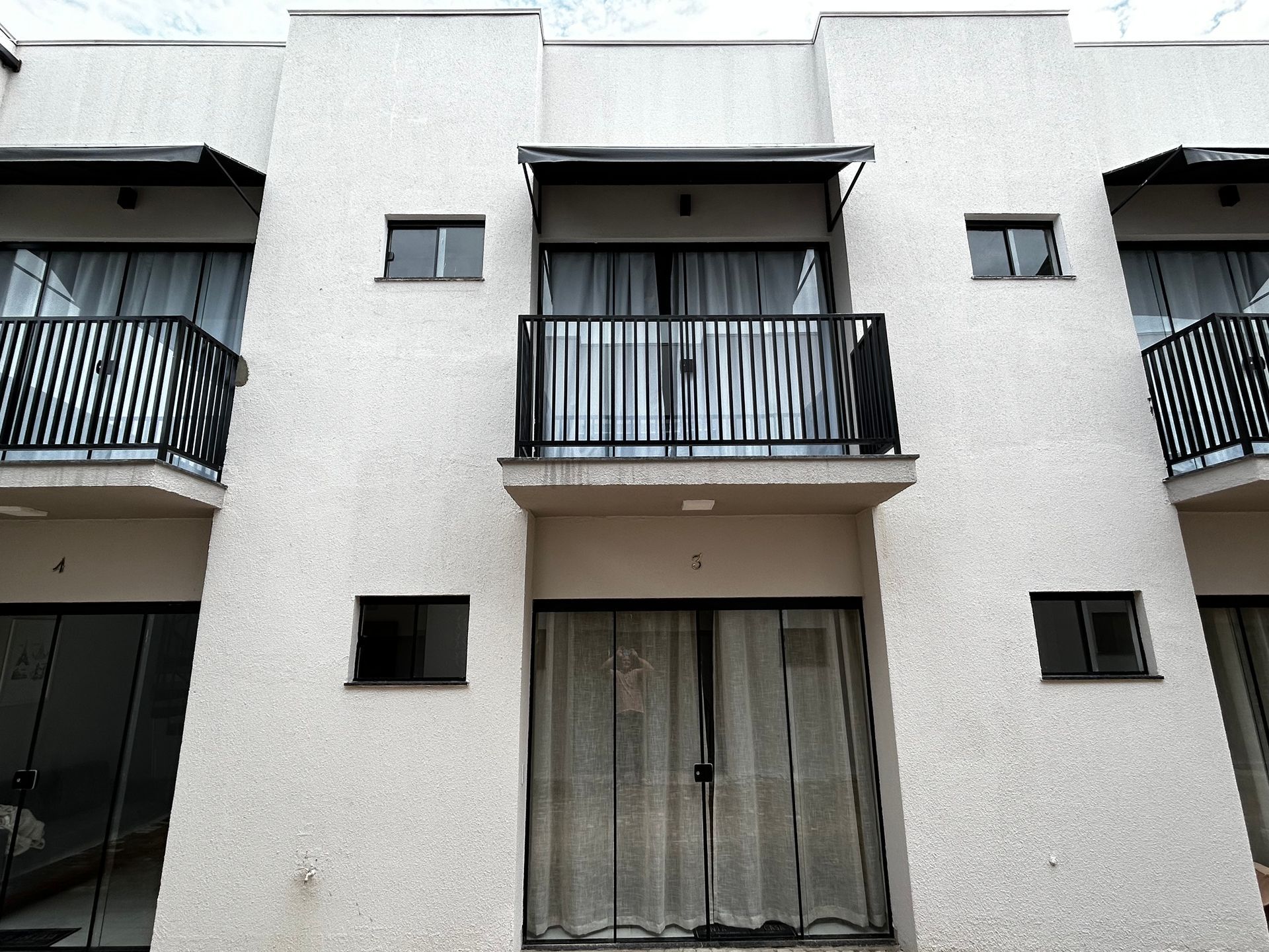 Fileira de casas geminadas bege com varandas e grades pretas, sob um céu nublado.