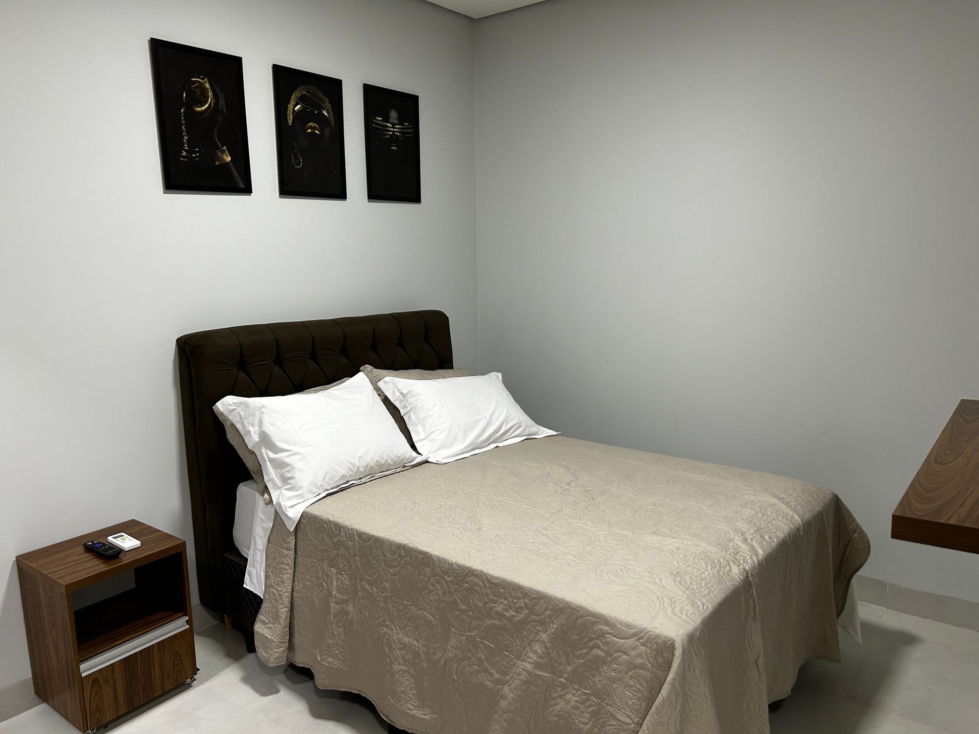 Quarto com cama de casal, criado-mudo e arte na parede. O quarto tem cores neutras.