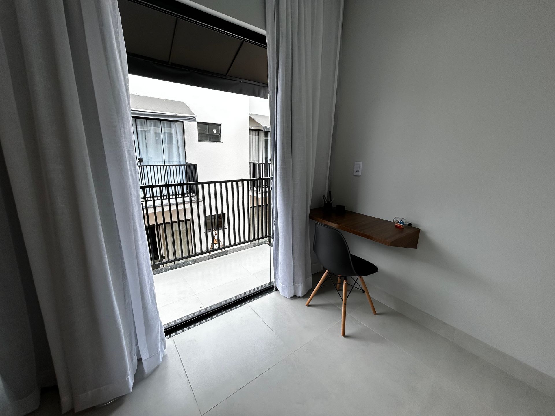 Quarto interno com varanda. Uma escrivaninha e uma cadeira ficam perto das portas abertas.