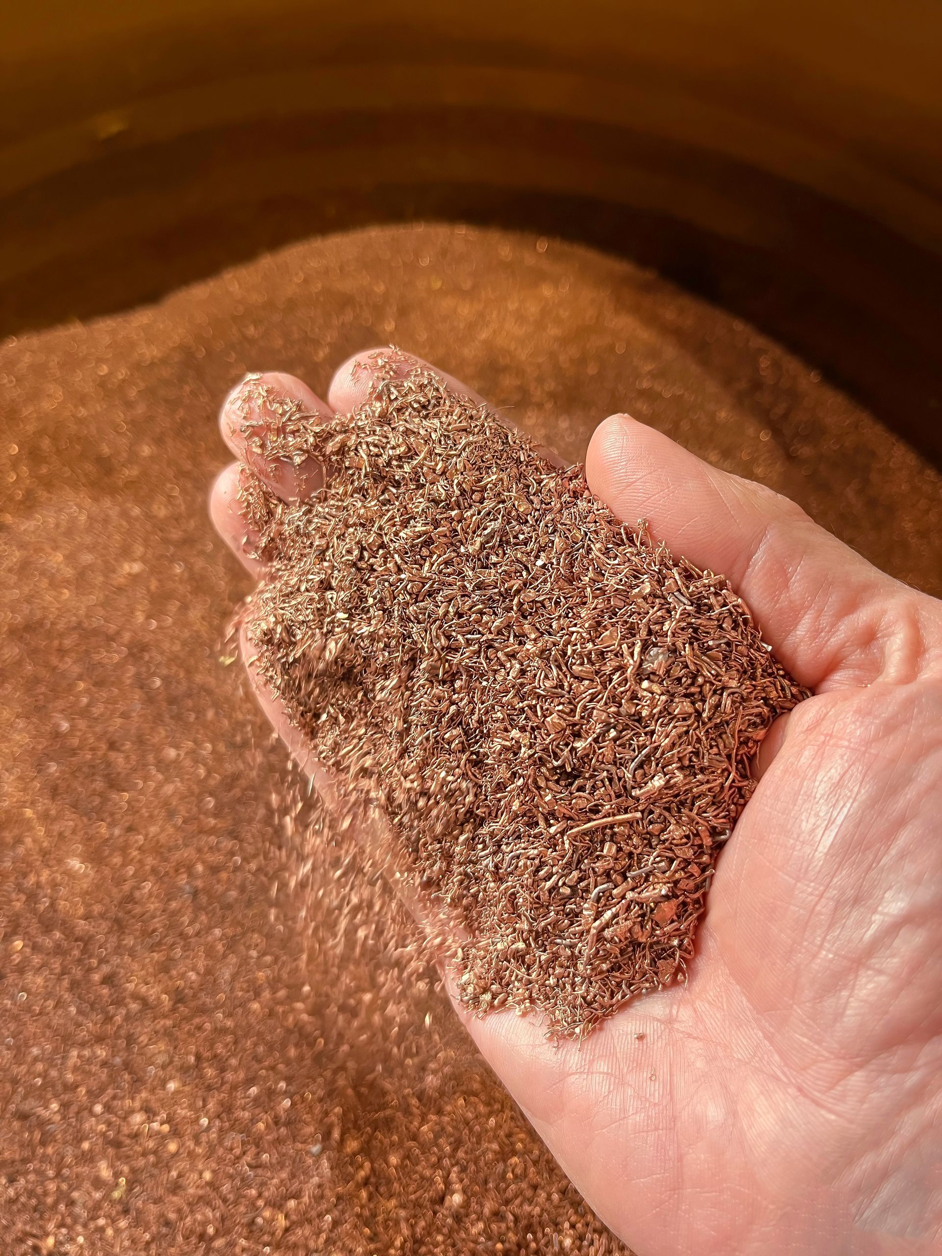 A person is holding a pile of brown sand in their hand.