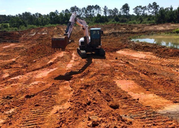 An excavator is moving dirt in a field with trees in the background