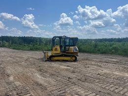 A yellow bulldozer is driving through a dirt field.