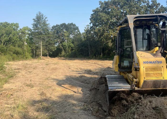 A yellow komatsu bulldozer is driving through a dirt field.