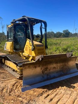 A yellow bulldozer is driving through a dirt field.