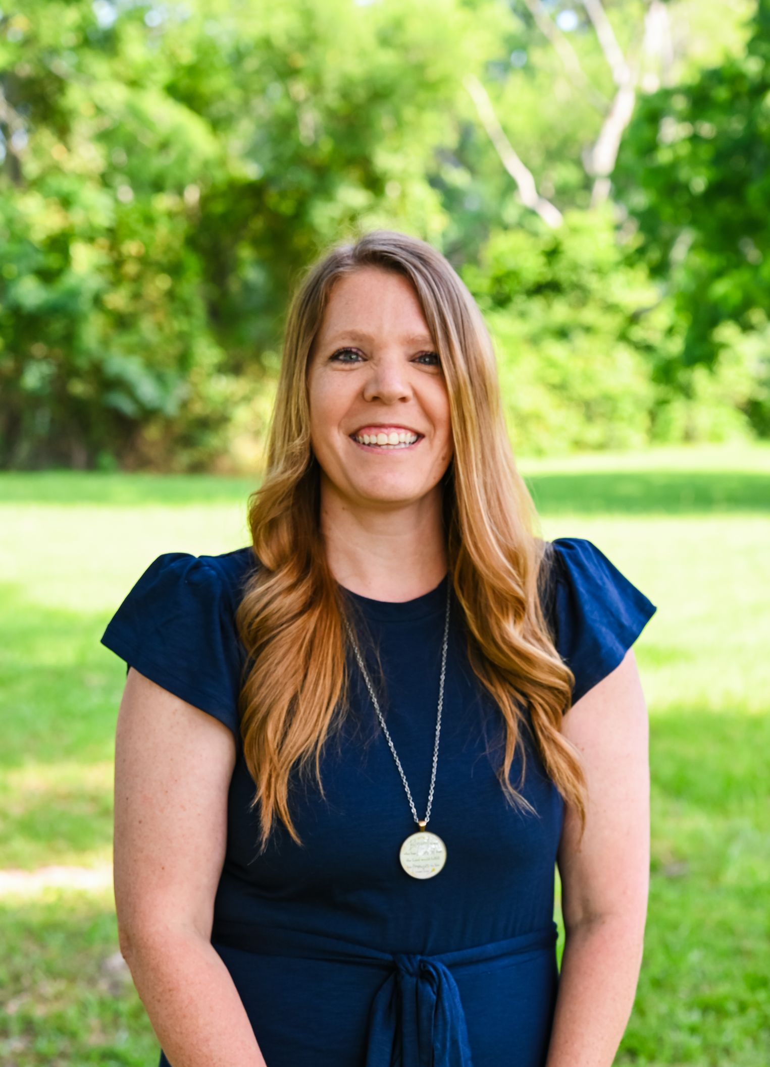 Smiling woman in a navy dress standing outdoors in front of green trees