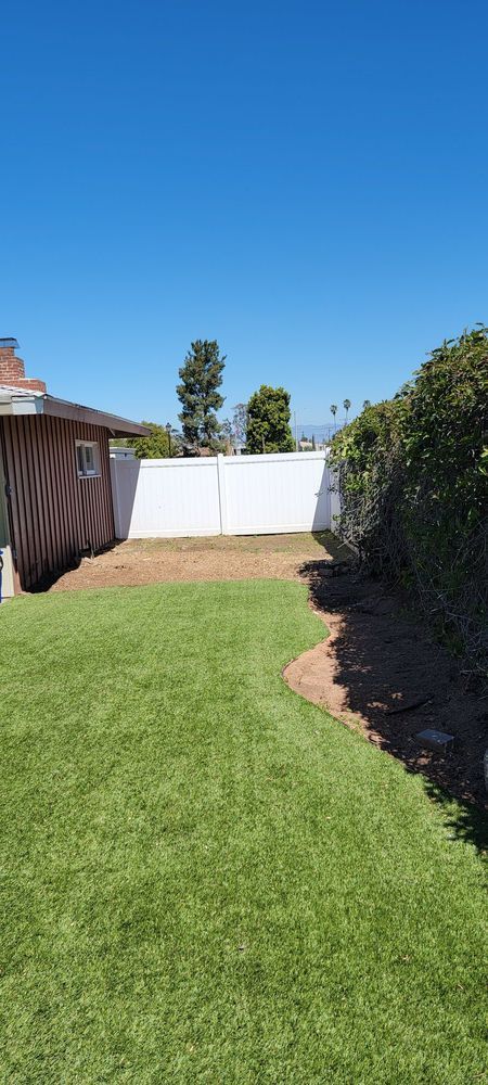 A backyard with a lush green lawn and a white fence.