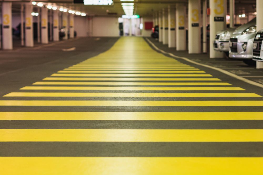 Yellow and black striped crosswalk in parking garage, cars parked on the right.