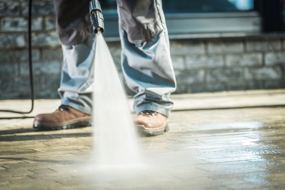 Person using a pressure washer, cleaning a brick patio. Water spraying from the nozzle, splashing.