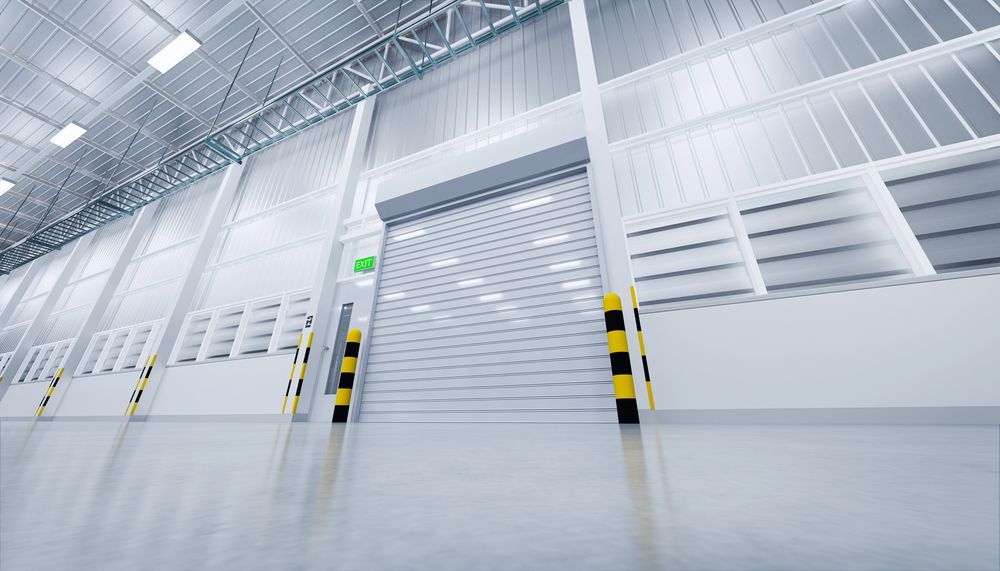 Inside of a large, empty warehouse; a roll-up door is closed, with windows above.