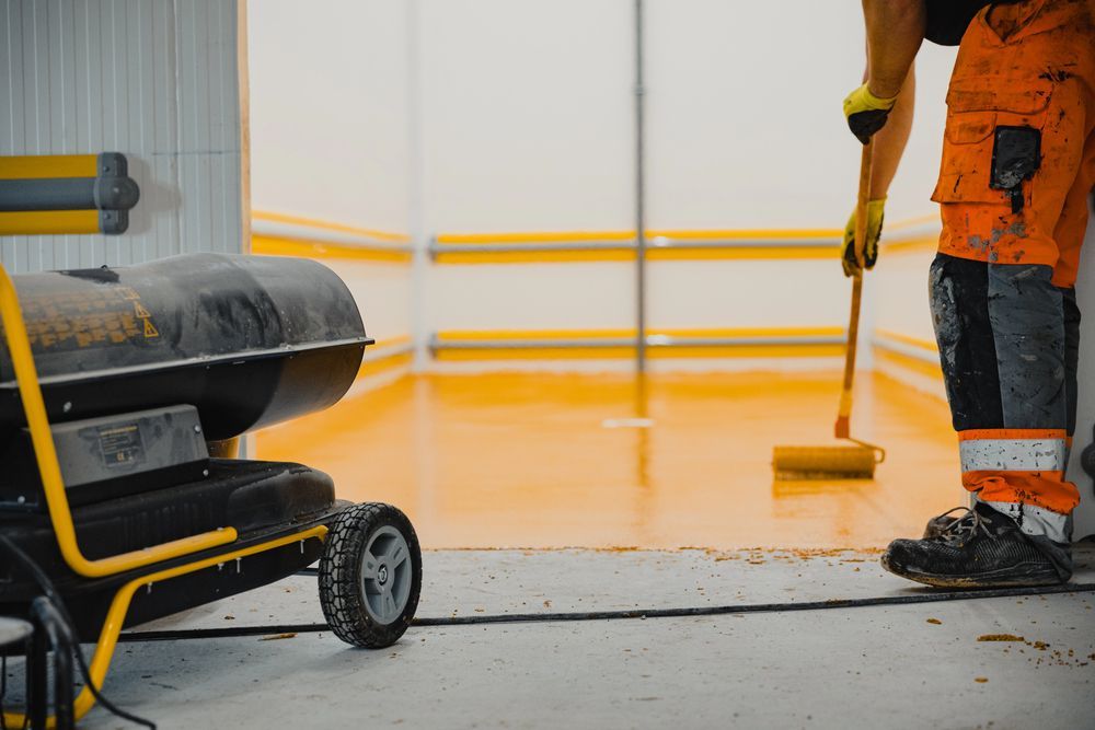 Person in orange workwear rolling orange epoxy on a floor, near a heater.