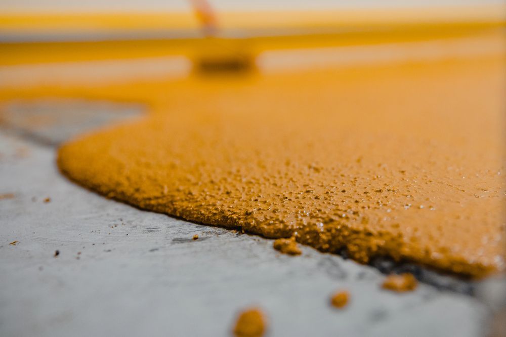 Close-up of orange epoxy flooring being spread on a gray concrete surface.