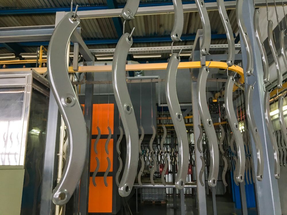 Metal parts on a conveyor line coated in gray paint inside an industrial setting.