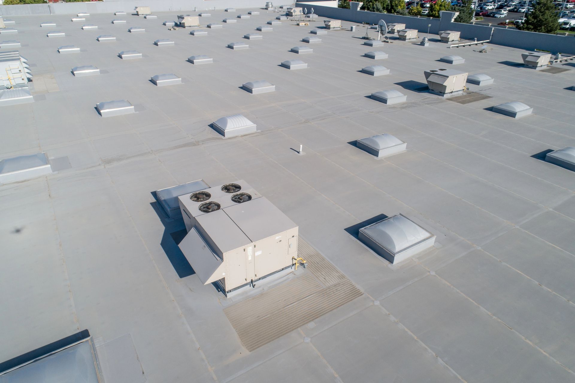Aerial view of a flat commercial roof with HVAC units, skylights, and vents, colored in white and gray.