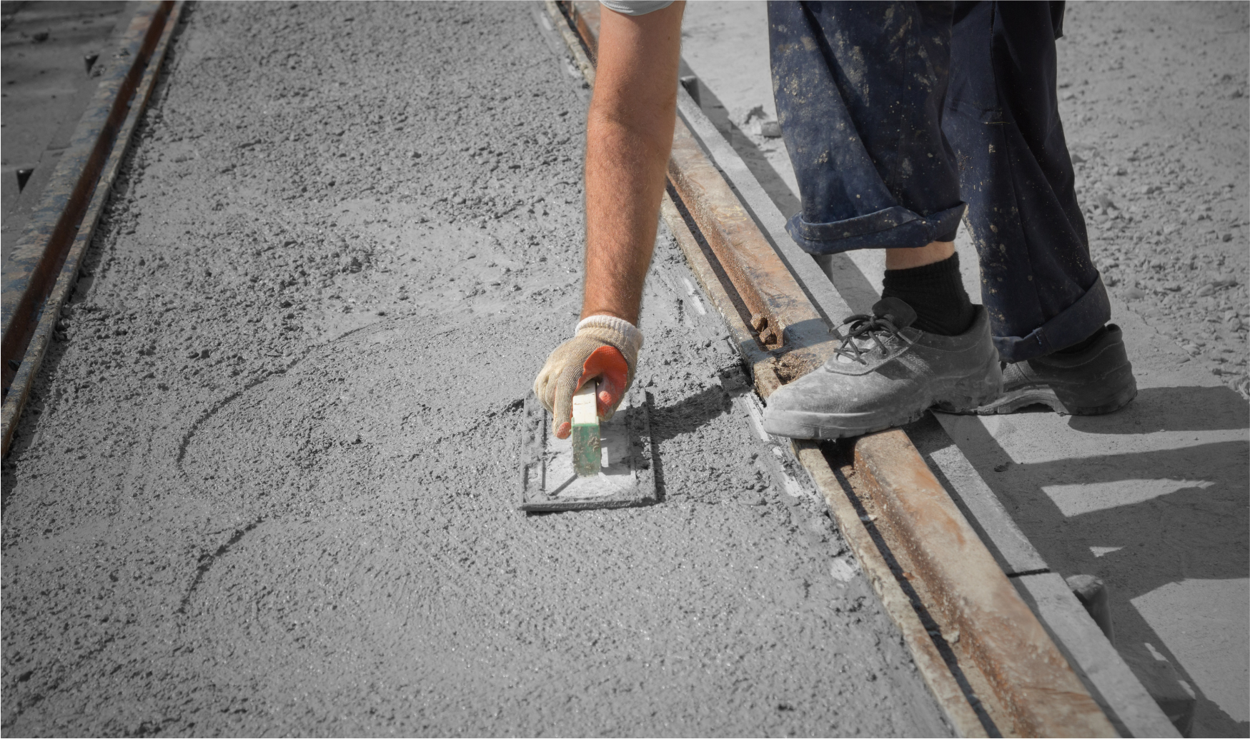 Person smoothing wet concrete with a trowel near metal track.