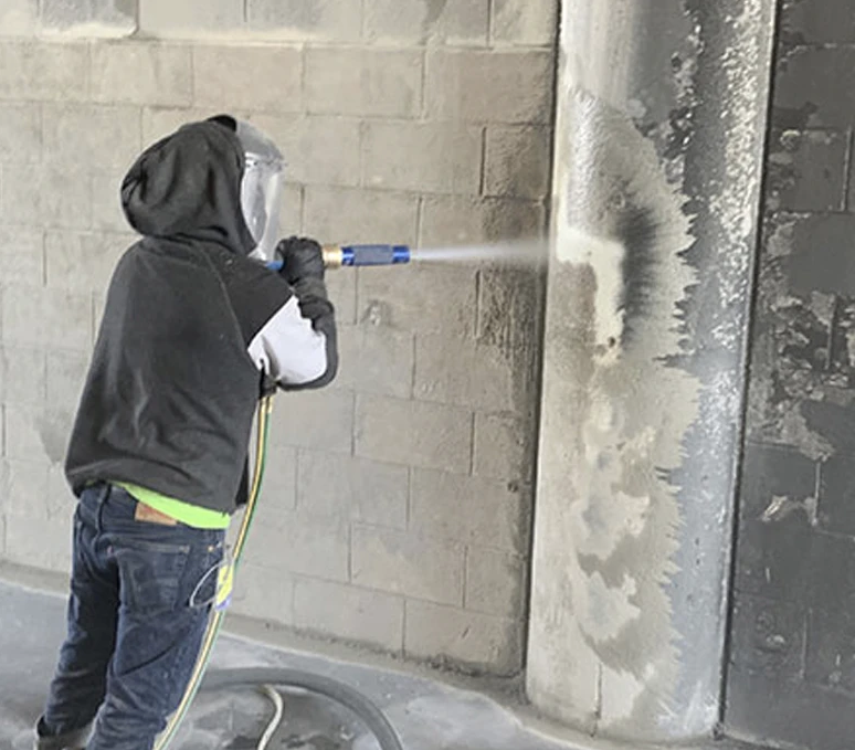 Machine spraying white material in a room with windows; floor and machine covered in powder.
