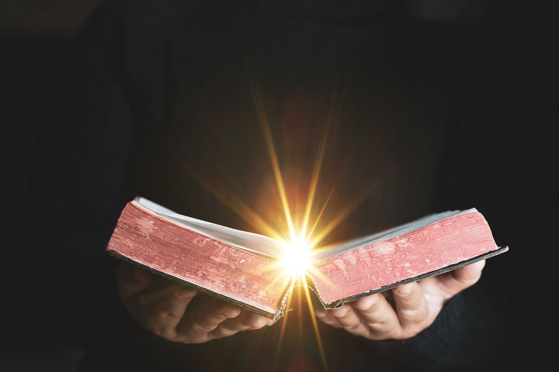 A person is holding a bible with a light coming out of it.